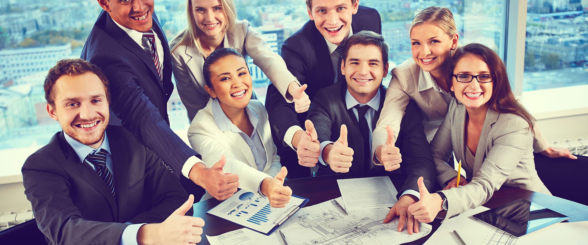 Group of business partners showing thumbs up while sitting at workplace in office